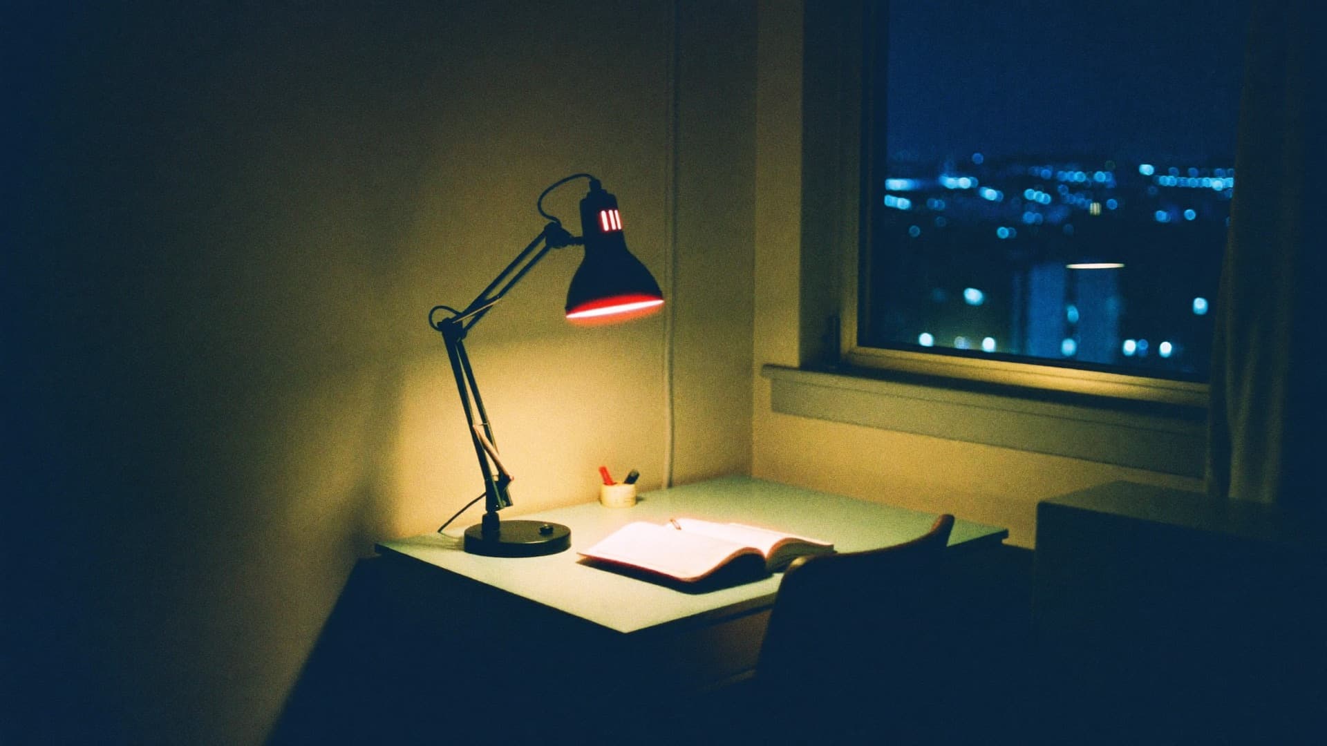 Quarto de estudante iluminado só pela luminária, madrugada